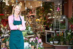 A smiling woman standing in front of a floral shop with arms crossed